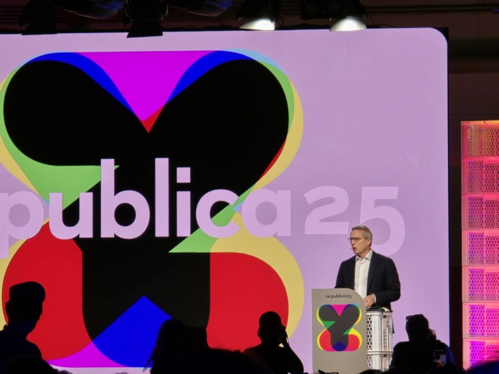 Ein Mann im Anzug spricht auf einer Bühne vor einer großen Leinwand mit dem re:publica25-Logo.